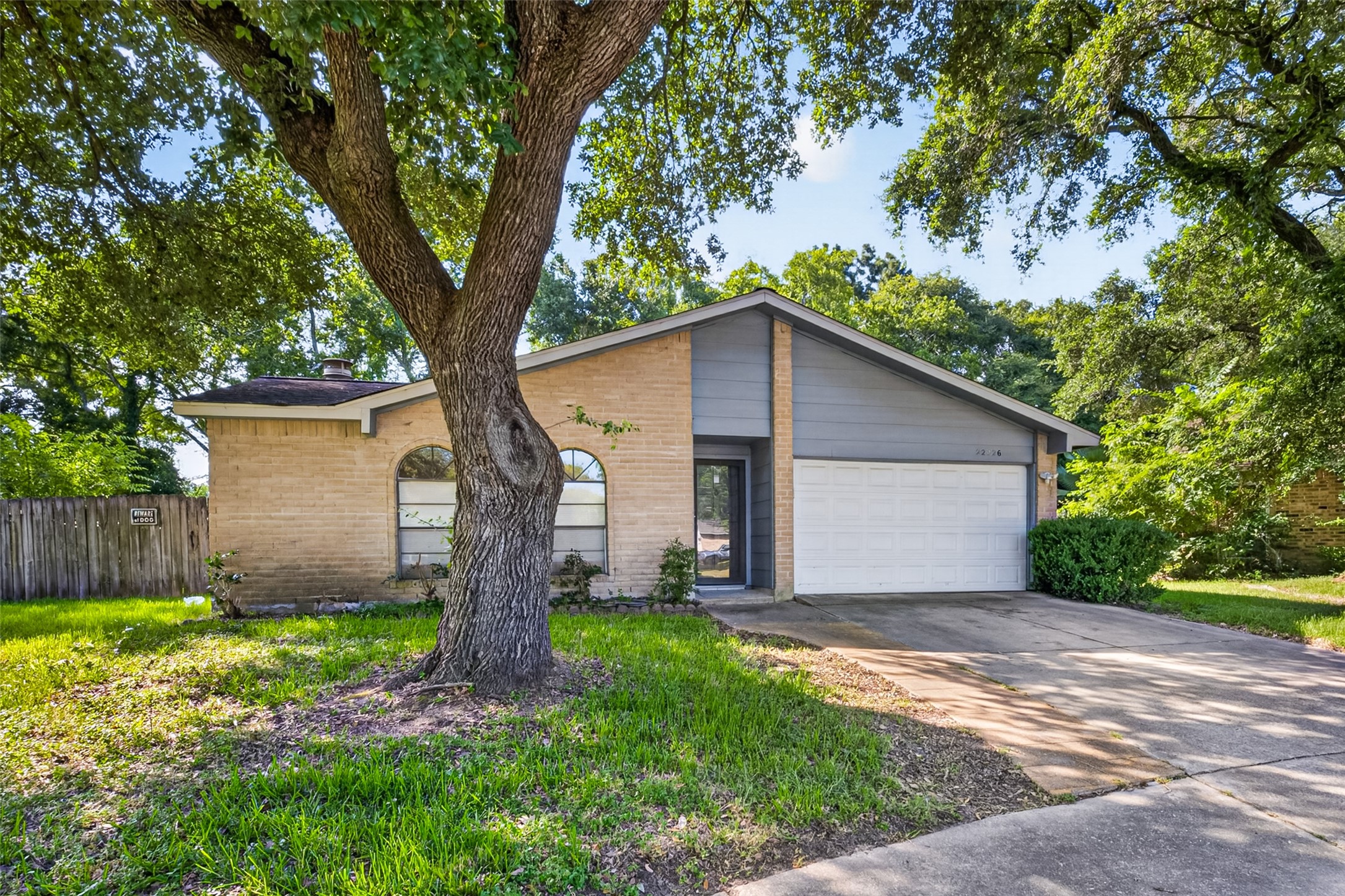 22926 Millgate Drive Spring, TX 77373 - Photo 2 of 34 Charming single-story home with a brick facade and pitched roof, featuring a two-car garage. The front yard is shaded by a mature tree, providing a welcoming entrance.