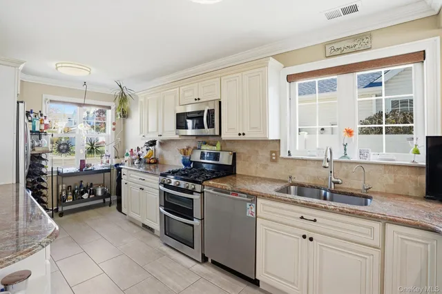 a large kitchen with stainless steel appliances granite countertop a stove top oven a sink a refrigerator and white cabinets