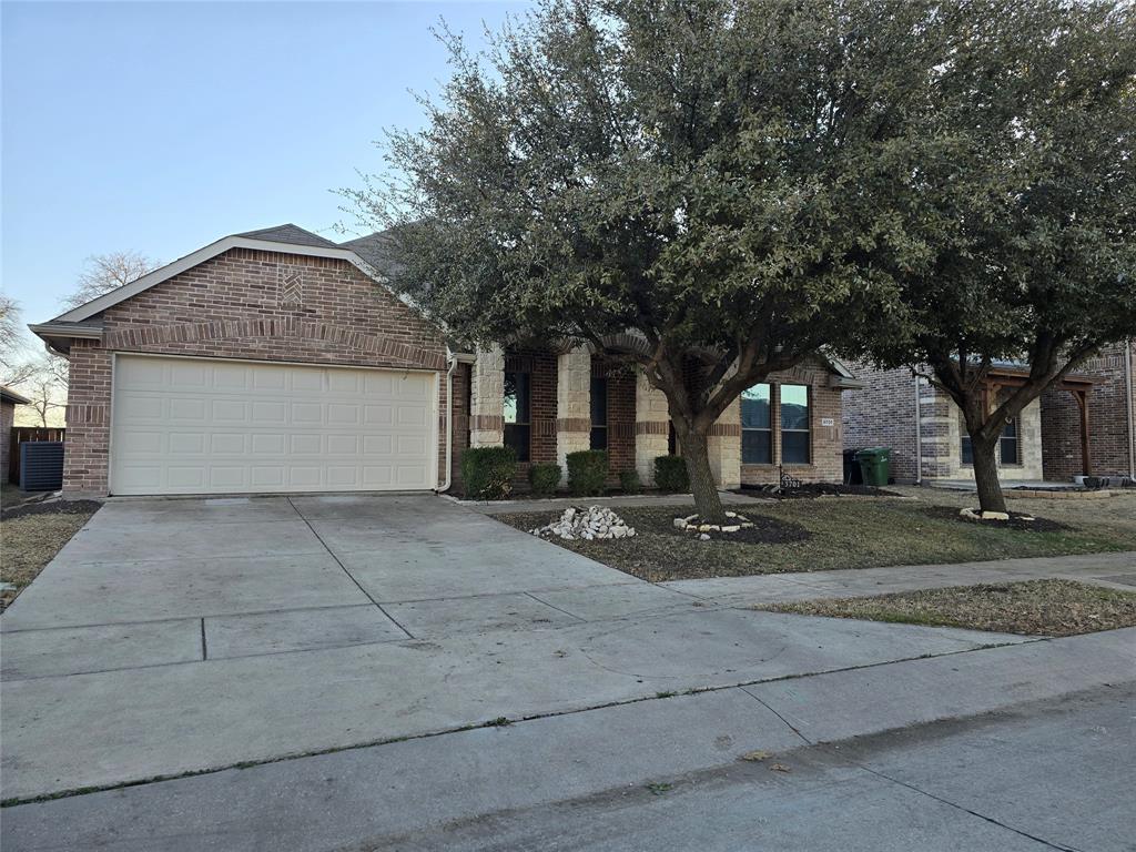 View of front facade featuring a garage, brick siding, driveway, and central AC