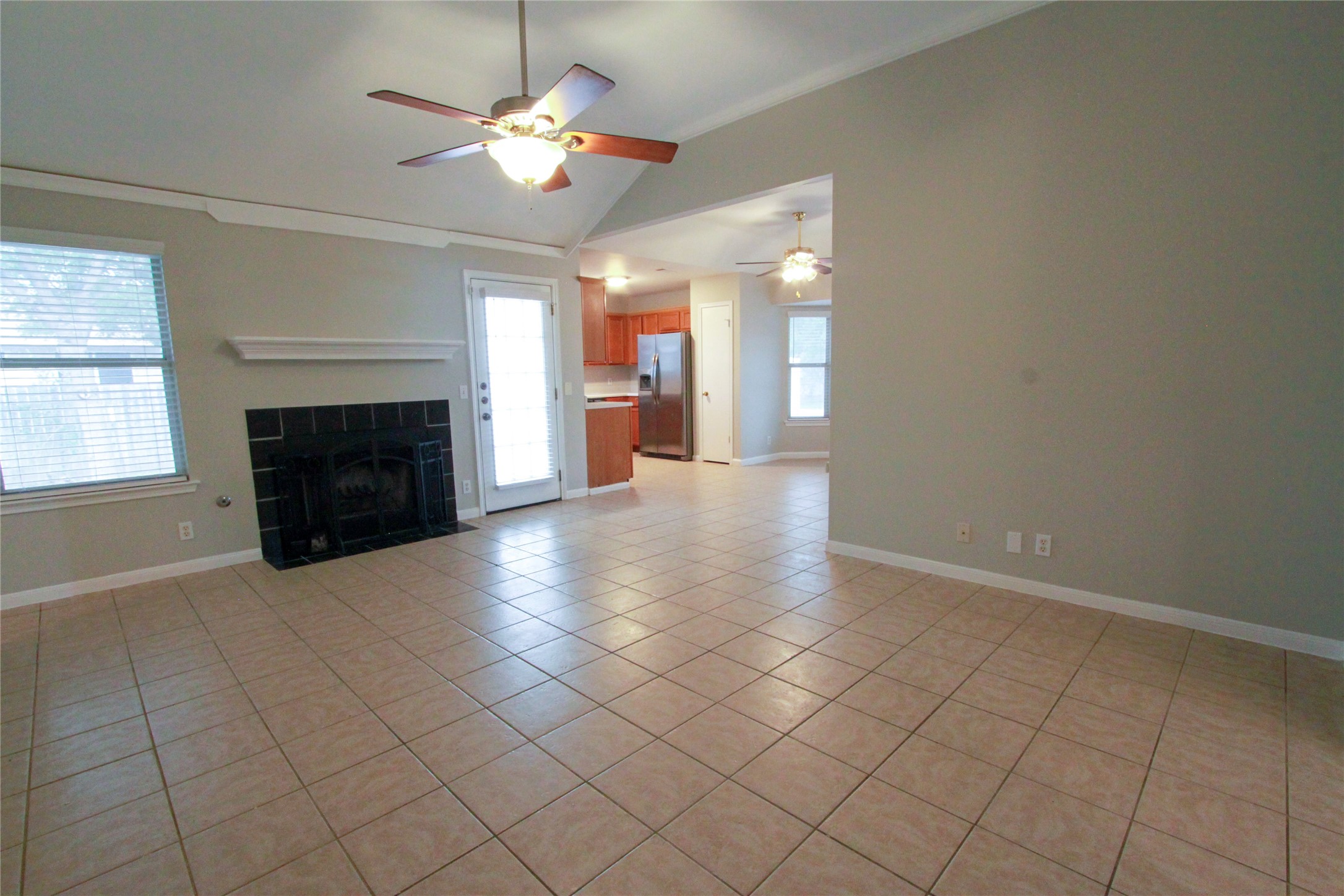 14708 Highsmith Street Austin, TX 78725 - Photo 6 of 28 Unfurnished living room featuring a tile fireplace, light tile patterned floors, a ceiling fan, and vaulted ceiling