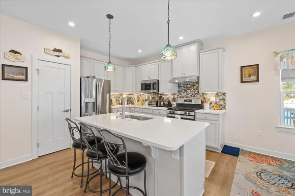 a kitchen with stainless steel appliances kitchen island a refrigerator a stove a sink a dining table and chairs with wooden floor