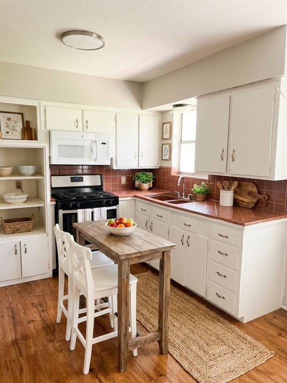 1910 Mercedes Road Denton, TX 76205 - Photo 2 of 5 Kitchen with tile countertops, white microwave, white cabinets, light wood-style floors, and stainless steel range with gas cooktop