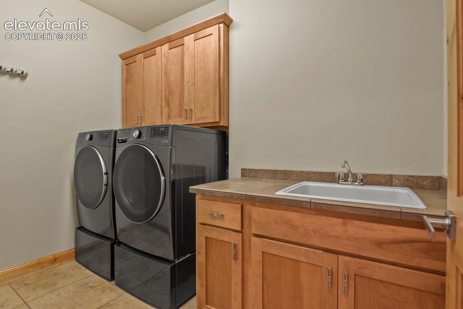 5545 Wilson Road Colorado Springs, CO 80919 - Photo 25 of 48 Laundry area featuring wood-finish cabinetry, a utility sink with a stainless steel faucet, and tile flooring