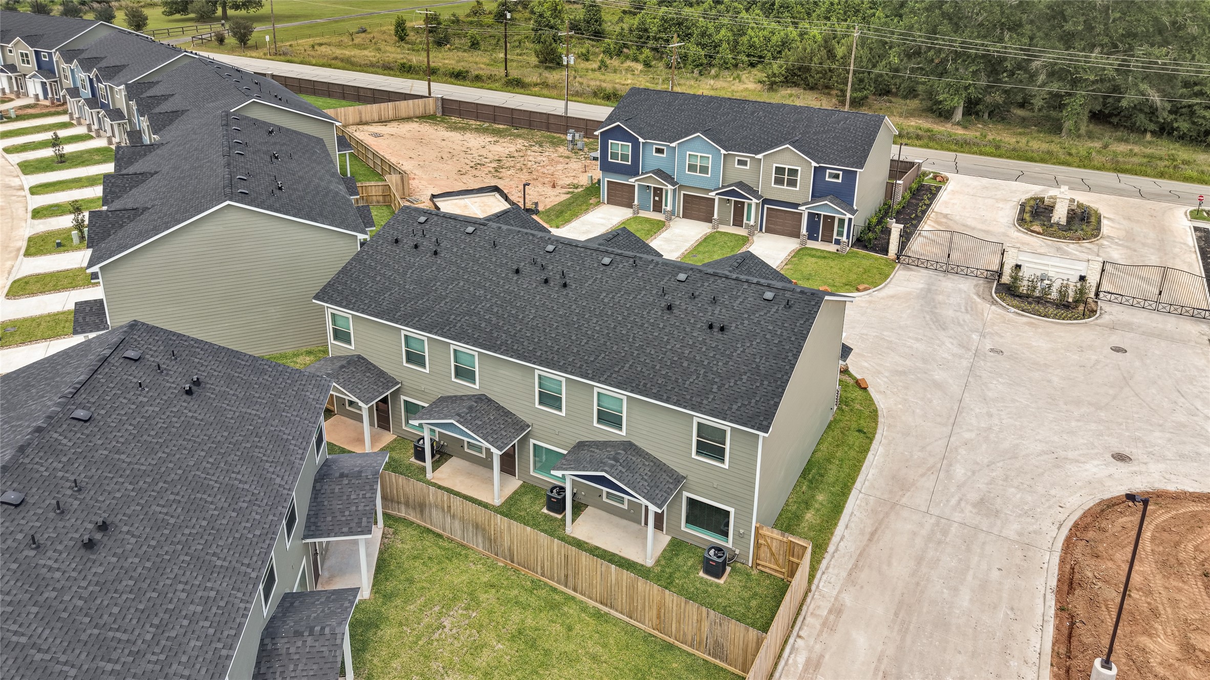 14010 Longstreet Road, Unit 2 Willis, TX 77318 - Photo 7 of 29 This photo shows a modern townhouse community with neatly arranged units featuring two-story designs and dark roofs. The neighborhood includes well-maintained lawns, private backyards with fencing, and a gated entrance, offering a sense of security and privacy. The area is surrounded by greenery, providing a pleasant suburban atmosphere.