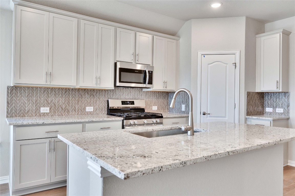 13709 Tucker Hedge Pass Elgin, TX 78621 - Photo 2 of 14 Kitchen featuring decorative backsplash, appliances with stainless steel finishes, light stone countertops, a kitchen island with sink, and light wood-style flooring
