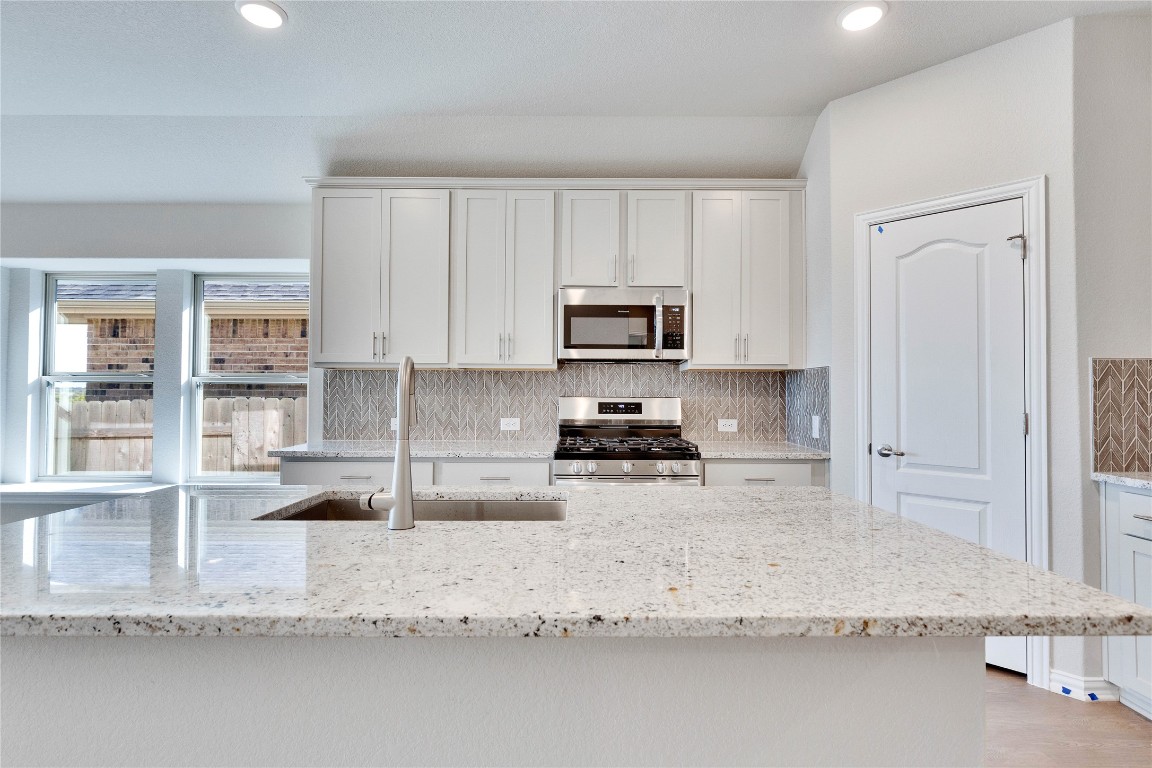 13709 Tucker Hedge Pass Elgin, TX 78621 - Photo 3 of 14 Kitchen featuring decorative backsplash, white cabinetry, light stone counters, stainless steel appliances, and recessed lighting