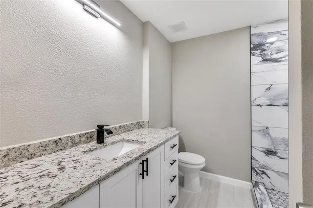 a bathroom with a granite countertop sink a toilet and a shower