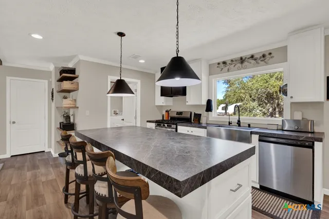 a kitchen with stainless steel appliances kitchen island granite countertop a refrigerator oven a sink dishwasher and white cabinets with wooden floor