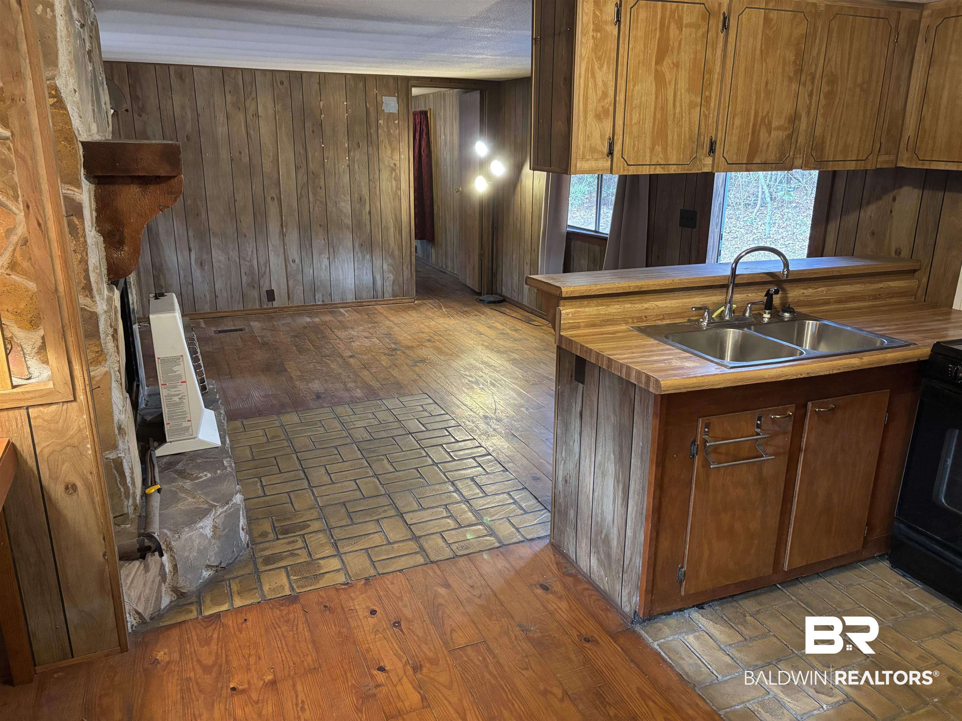 15575 Rogers Drive Chunchula, AL 36521 - Photo 22 of 42 Kitchen featuring brick floor, wooden walls, a sink, light countertops, and brown cabinetry