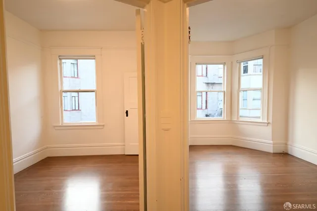 a view of an empty room with wooden floor and a window