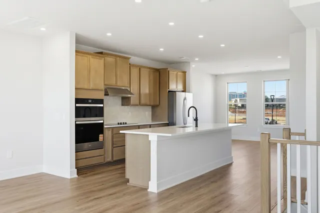 a large kitchen with stainless steel appliances granite countertop a stove a sink a refrigerator and white cabinets with wooden floor