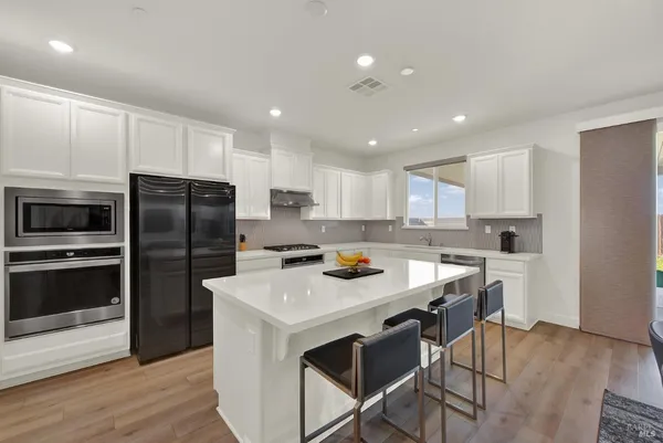 a view of a kitchen with kitchen island a stove a sink a refrigerator and a living room with wooden floor