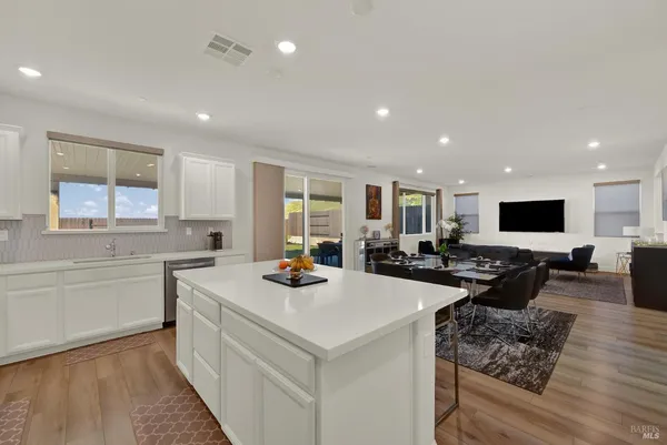 a kitchen with stainless steel appliances a stove a sink a refrigerator white cabinets and wooden floor