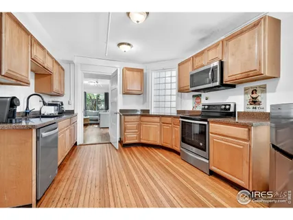 a kitchen with stainless steel appliances granite countertop wooden cabinets a sink dishwasher a stove and a refrigerator with wooden floor