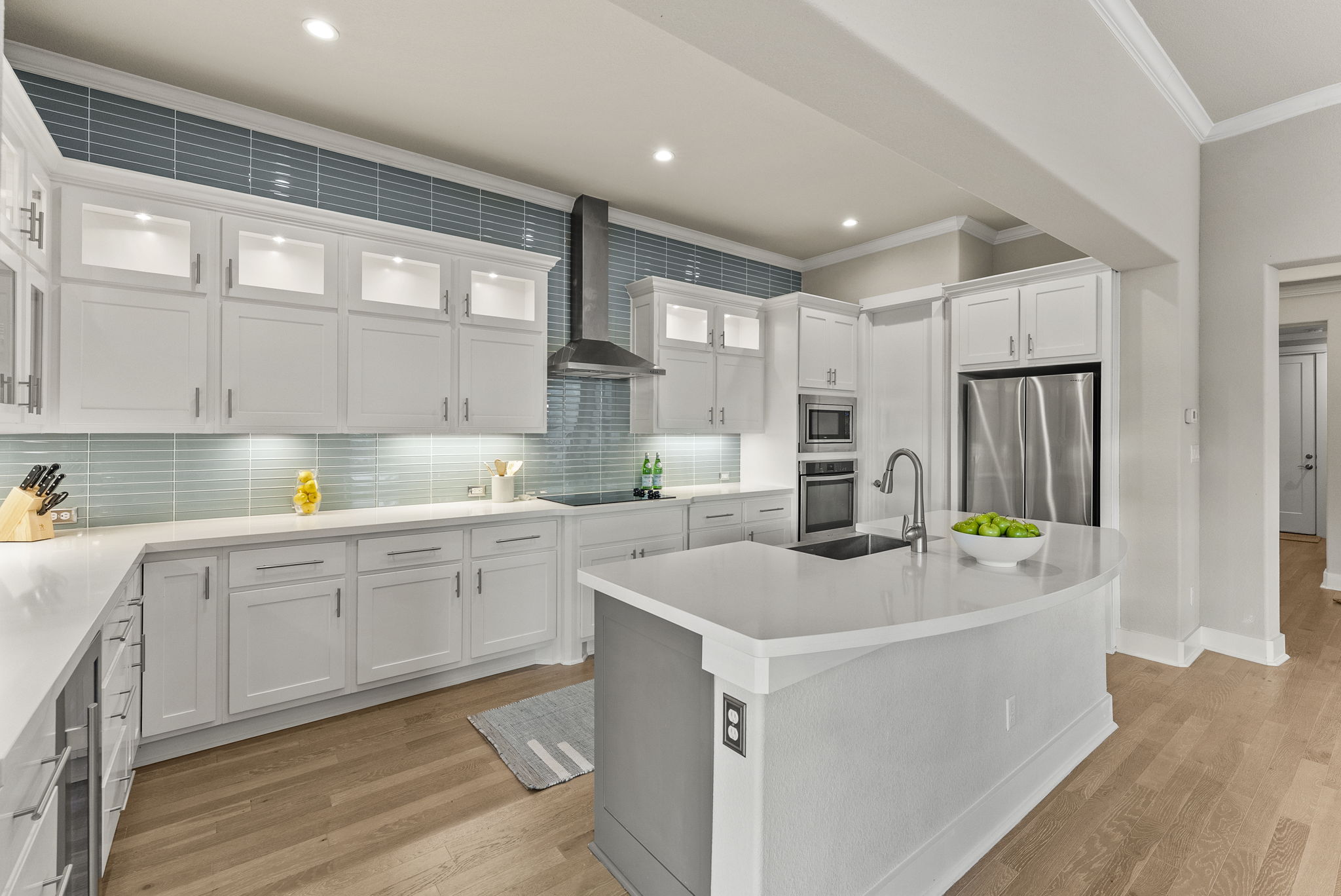 5502 Patagonia Pass Austin, TX 78738 - Photo 11 of 34 Kitchen featuring glass insert cabinets, ornamental molding, white cabinetry, wall chimney range hood, and light wood-style floors