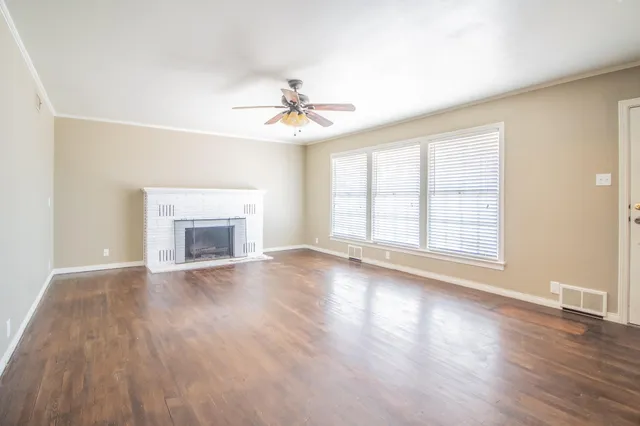 an empty room with wooden floor fireplace and windows