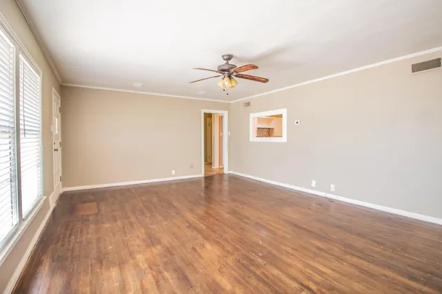 an empty room with wooden floor ceiling fan and windows