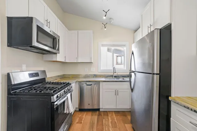 a kitchen with stainless steel appliances granite countertop a stove top oven a refrigerator a sink and dishwasher with wooden floor