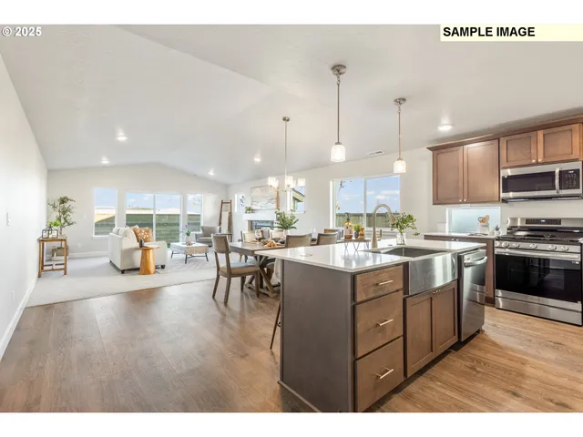 a kitchen with stainless steel appliances granite countertop a refrigerator a sink dishwasher a oven and a dining table with wooden floor