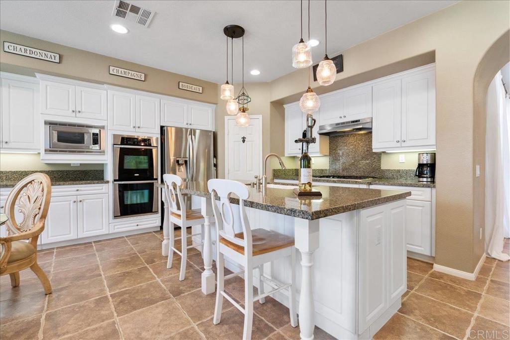 2667 Fallsview Road San Marcos, CA 92078 - Photo 21 of 54 a kitchen with stainless steel appliances granite countertop a stove top oven a refrigerator a sink and a dining table with chairs