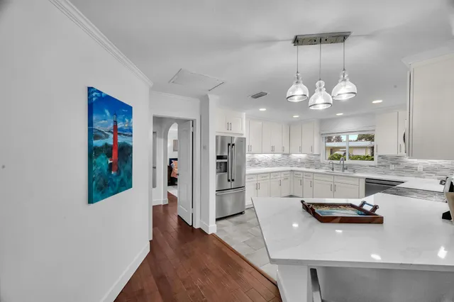 a kitchen with stainless steel appliances granite countertop a refrigerator a sink dishwasher a oven and a dining table with wooden floor