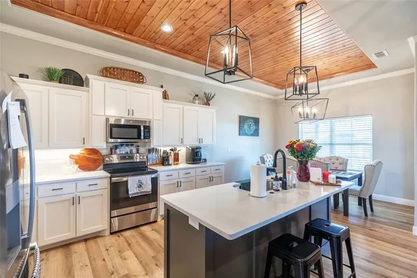 a kitchen with stainless steel appliances a stove a sink a refrigerator a dining table and chairs with wooden floor