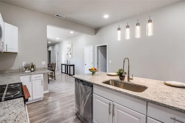 a kitchen with stainless steel appliances granite countertop a sink dishwasher and white cabinets with wooden floor