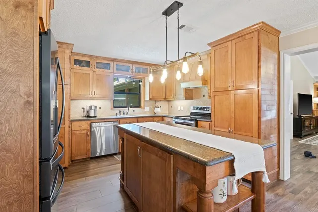 a kitchen with stainless steel appliances granite countertop a refrigerator a oven a sink and a dining table with wooden floor