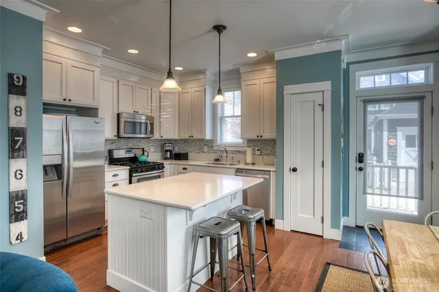 a kitchen with stainless steel appliances granite countertop a refrigerator a sink dishwasher a stove and white cabinets with wooden floor