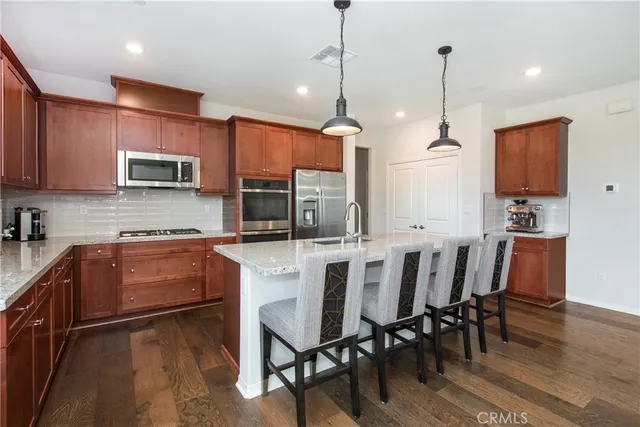 a kitchen with stainless steel appliances granite countertop a refrigerator a sink dishwasher a stove and white cabinets with wooden floor