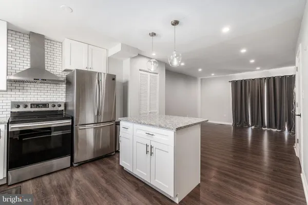 a kitchen with stainless steel appliances granite countertop a refrigerator a sink dishwasher a oven and a dining table with wooden floor