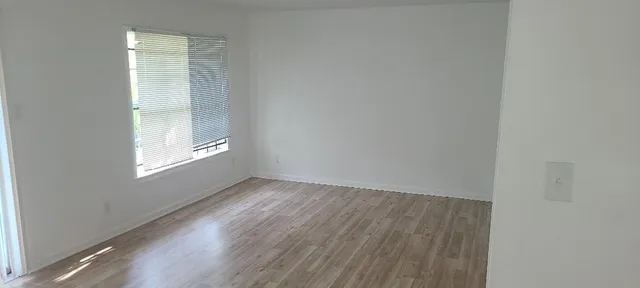 a view of an empty room with wooden floor and a window
