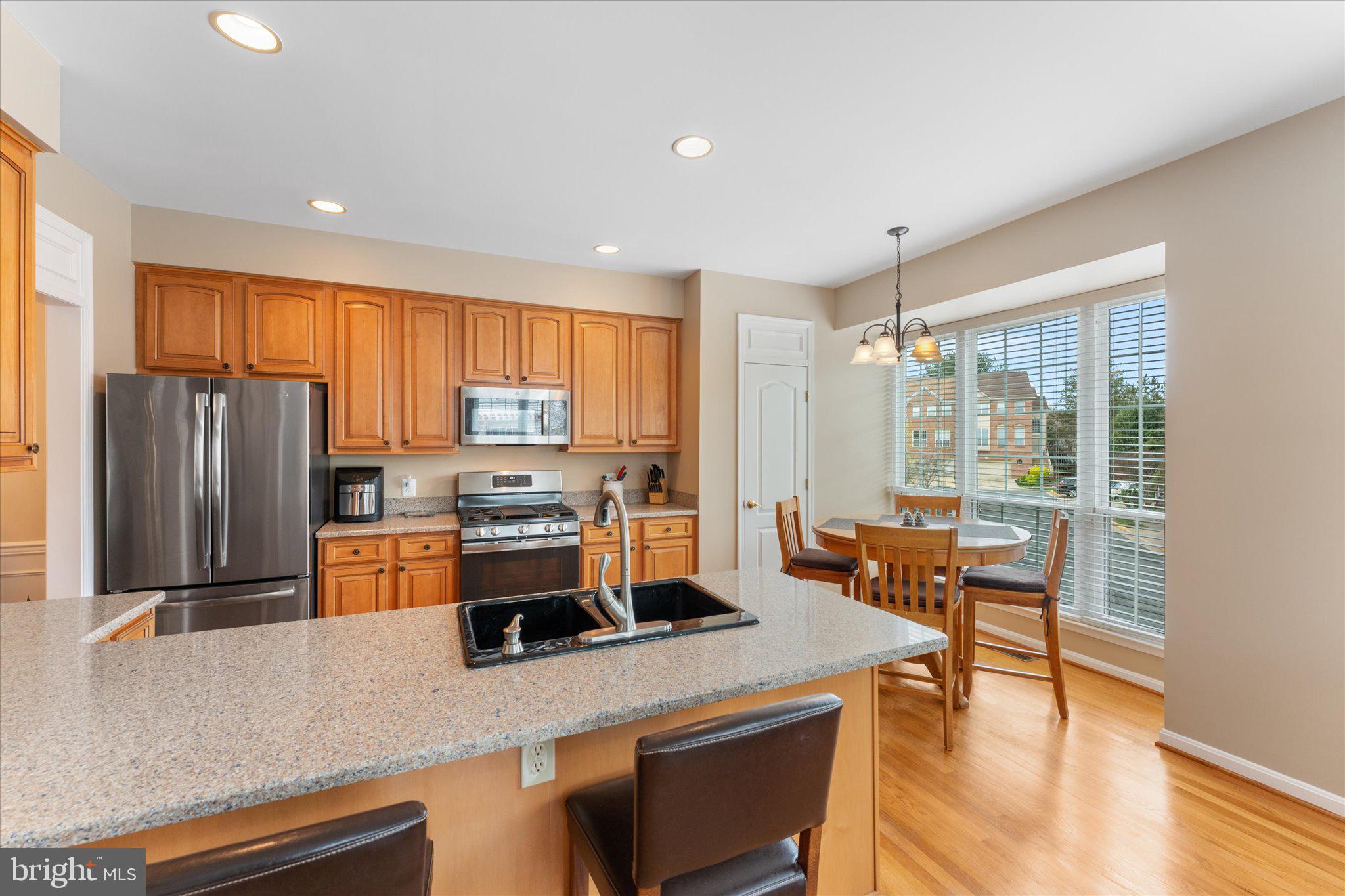 20900 Trinity Square Sterling, VA 20165 - Photo 29 of 46 a kitchen with stainless steel appliances granite countertop a stove a refrigerator a sink a dining table and chairs with wooden floor