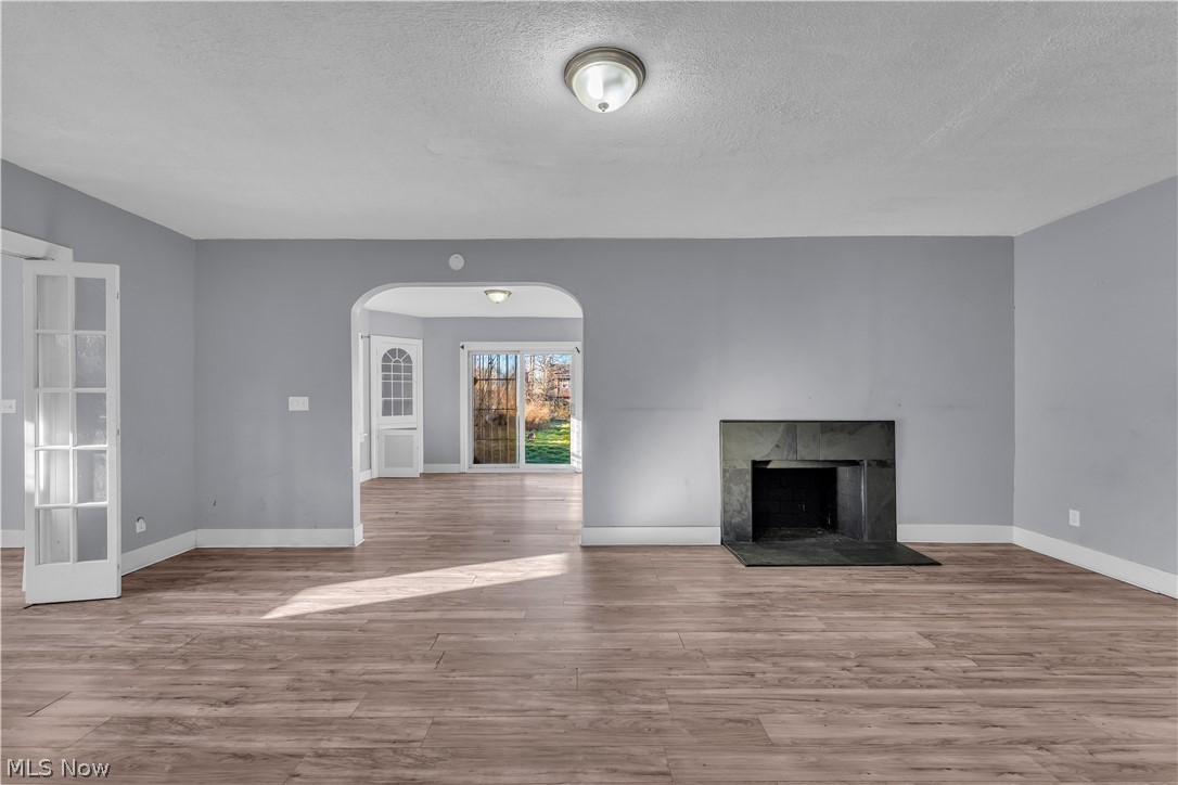 1858 Rudwick Road Cleveland, OH 44112 - Photo 7 of 36 Unfurnished living room with arched walkways, light wood-style flooring, a fireplace, and a textured ceiling