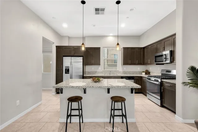 a kitchen with stainless steel appliances kitchen island granite countertop a sink a stove a refrigerator cabinets and chairs