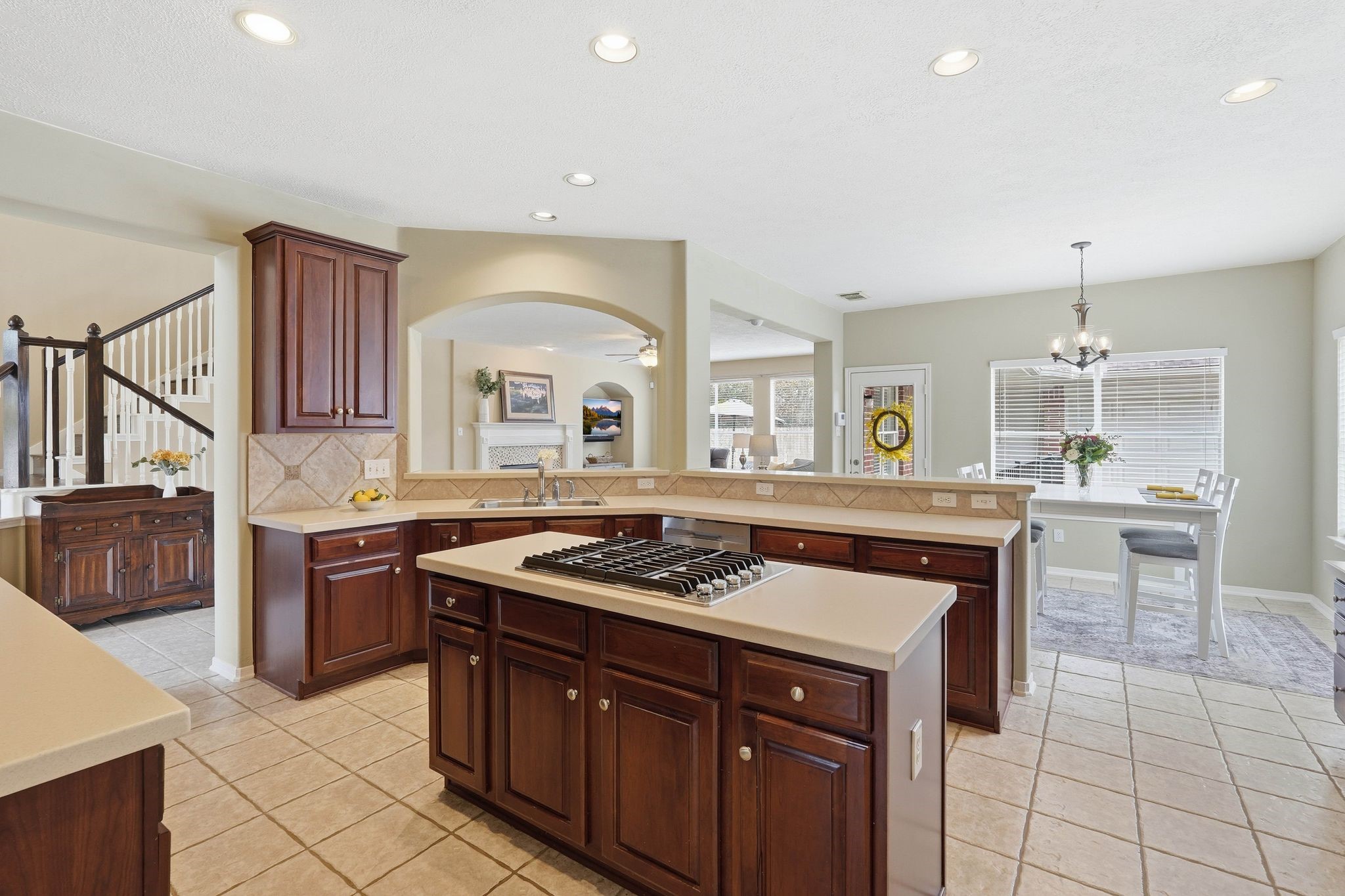 2515 Woodsboro Drive Spring, TX 77388 - Photo 13 of 44 This spacious, open-concept kitchen includes an island cooktop, ample counter space, and elegant dark wood cabinetry. It features tile flooring, recessed lighting, and a cozy dining area with large windows for natural light. The kitchen seamlessly connects to the living space, creating an inviting atmosphere for entertaining.