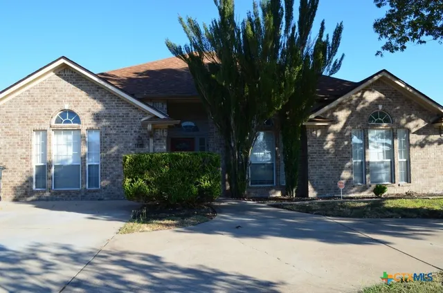 a view of a house with brick walls plants and large tree