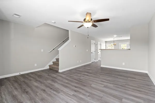 a view of an empty room with wooden floor and a ceiling fan