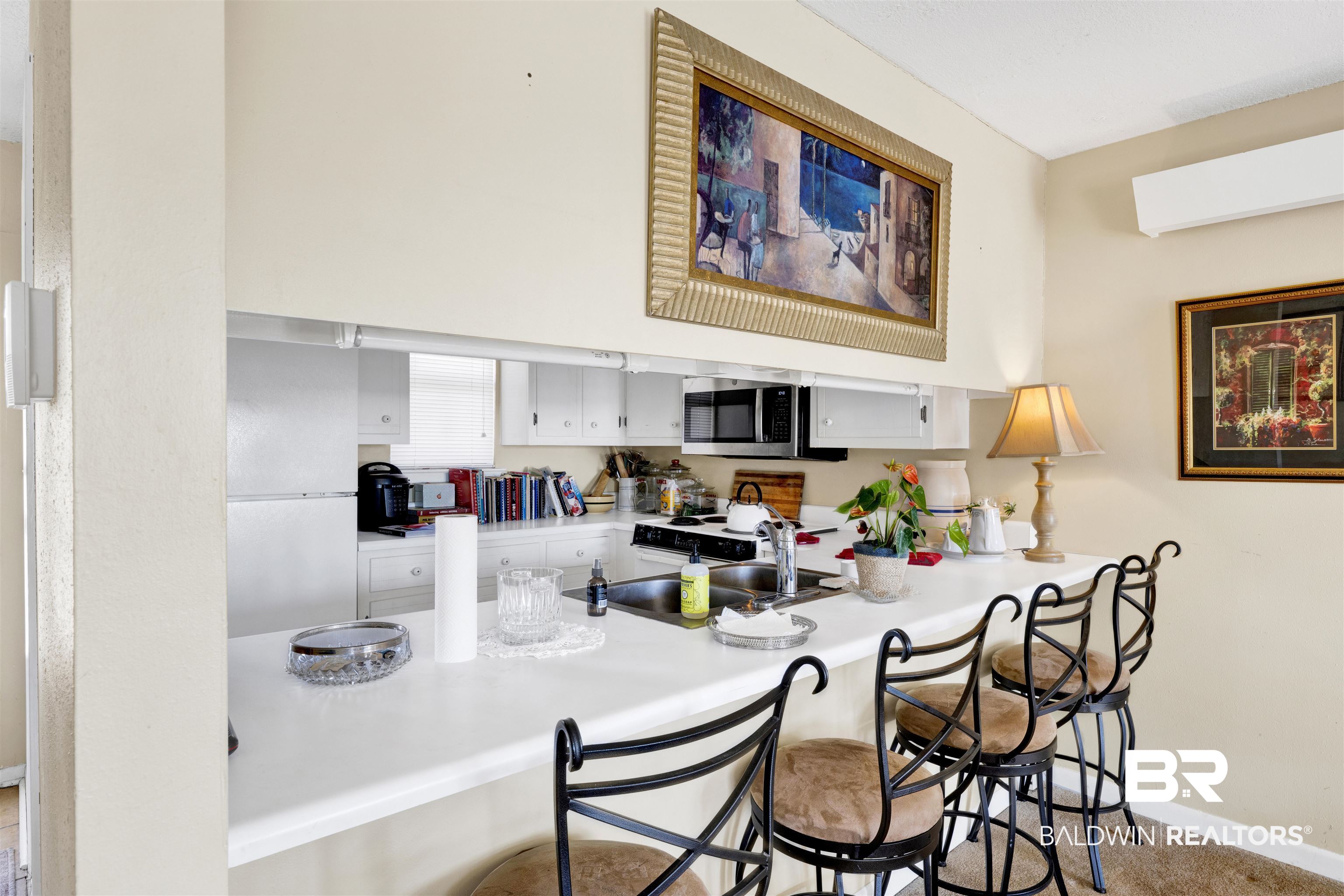 26222 Marina Road Orange Beach, AL 36561 - Photo 19 of 38 Kitchen featuring white cabinetry, a breakfast bar, light countertops, stainless steel microwave, and a peninsula