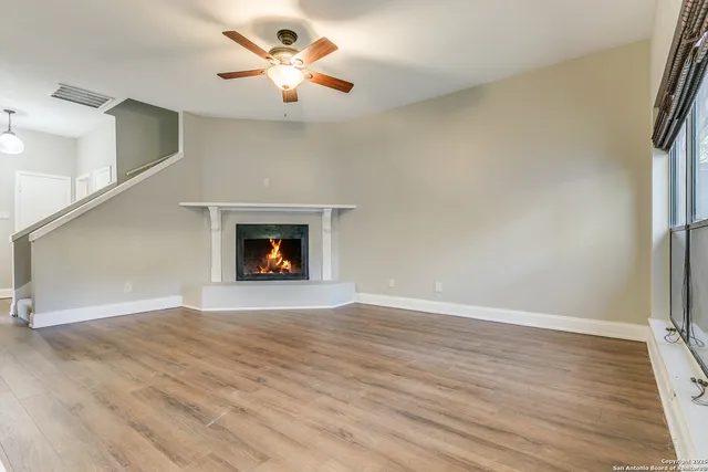 a view of an empty room with wooden floor fireplace and a window