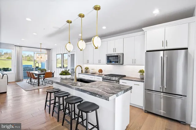 a kitchen with stainless steel appliances granite countertop a stove a refrigerator a kitchen island a dining table and chairs with wooden floor
