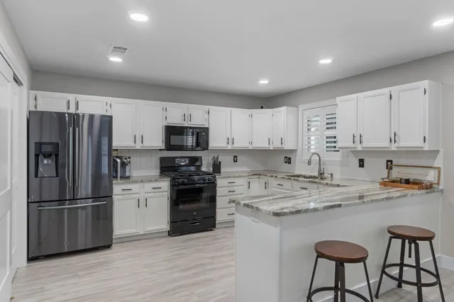 a kitchen with stainless steel appliances granite countertop a refrigerator a stove a sink dishwasher and white cabinets with wooden floor