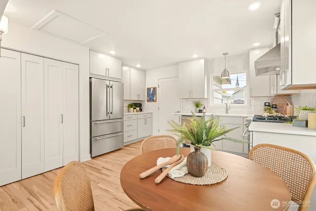 a kitchen with stainless steel appliances granite countertop a refrigerator a sink a dining table and chairs with wooden floor