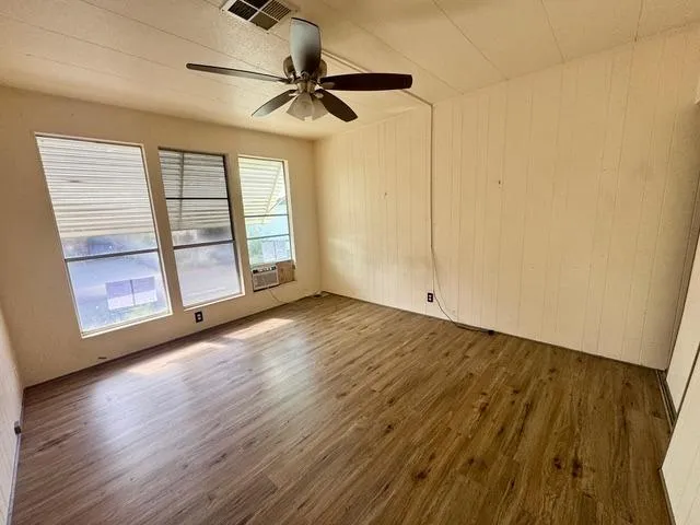 an empty room with wooden floor fan and windows