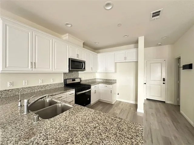 a kitchen with granite countertop a sink a stove a refrigerator and white cabinets