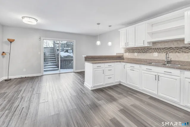 a large kitchen with granite countertop a stove top oven a sink dishwasher and white cabinets with wooden floor