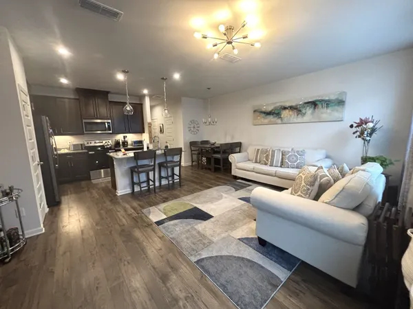 a living room with stainless steel appliances kitchen island granite countertop furniture a rug kitchen view and a chandelier