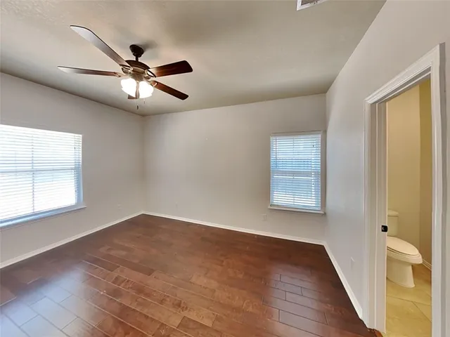 an empty room with wooden floor fan and windows