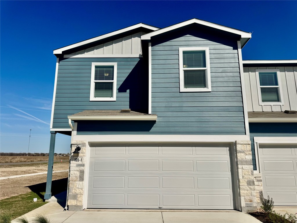 View of front of property with board and batten siding, stone siding, concrete driveway, and an attached garage