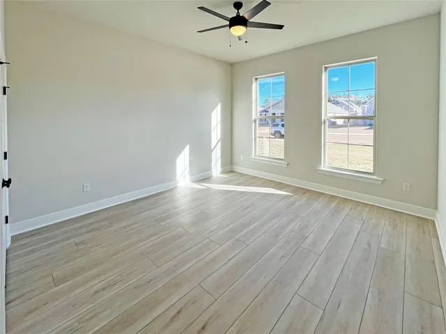 an empty room with wooden floor chandelier fan and windows